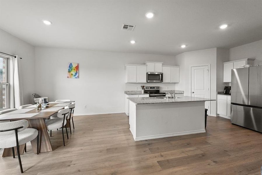 Open-concept kitchen and dining area featuring light wood-finish flooring, recessed lighting, and white cabinetry