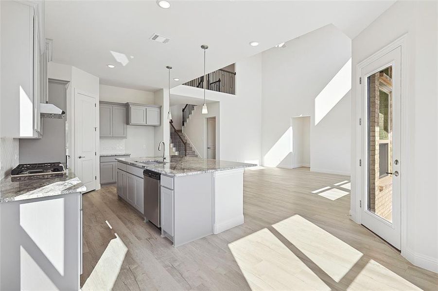 Kitchen featuring light hardwood / wood-style floors, decorative light fixtures, stainless steel dishwasher, and a center island with sink