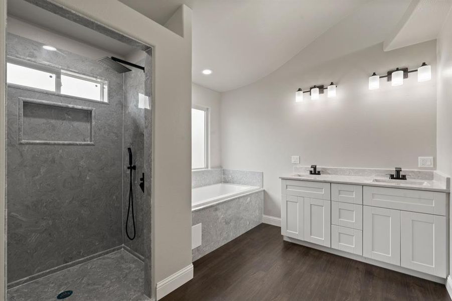 Bathroom featuring a bath, wood finished floors, vaulted ceiling, a walk in shower, and double vanity