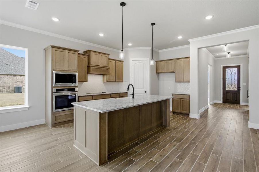 Kitchen with wood tiled floors, light stone counters, a kitchen island with sink, decorative light fixtures, and stainless steel appliances