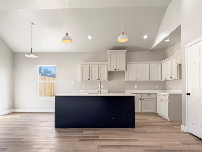 Dual tone kitchen featuring vaulted ceiling, pendant lighting, light wood finished floors, a center island with sink, and two tone color scheme Dual tone kitchen featuring vaulted ceiling, pendant lighting, light wood finished floors, a center island with sink, and two tone color scheme