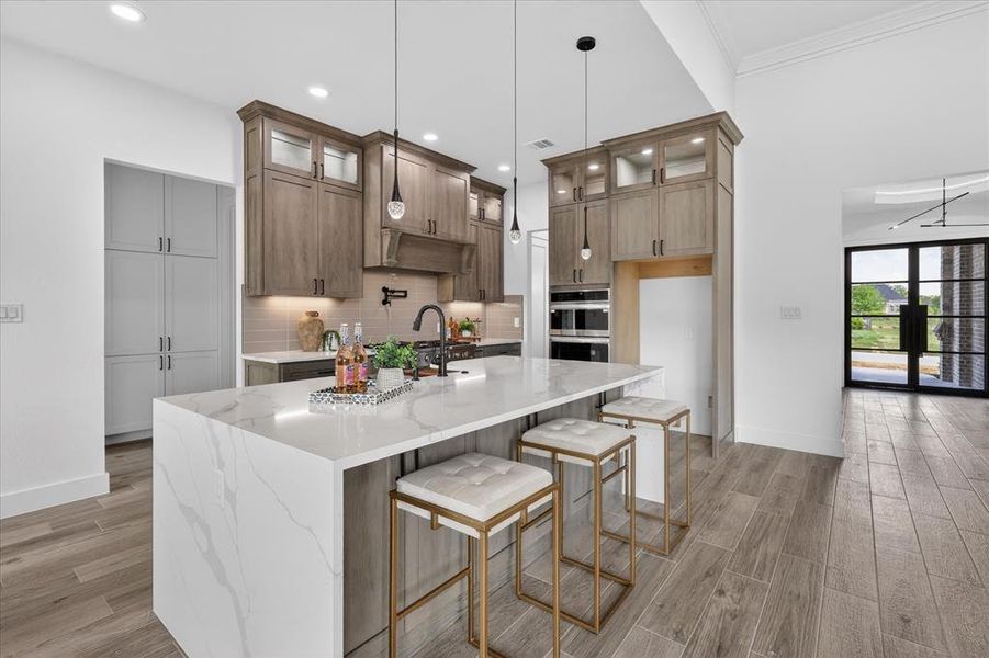 Kitchen with light stone counters, light wood-type flooring, a breakfast bar area, an island with sink, and glass fronted cabinets