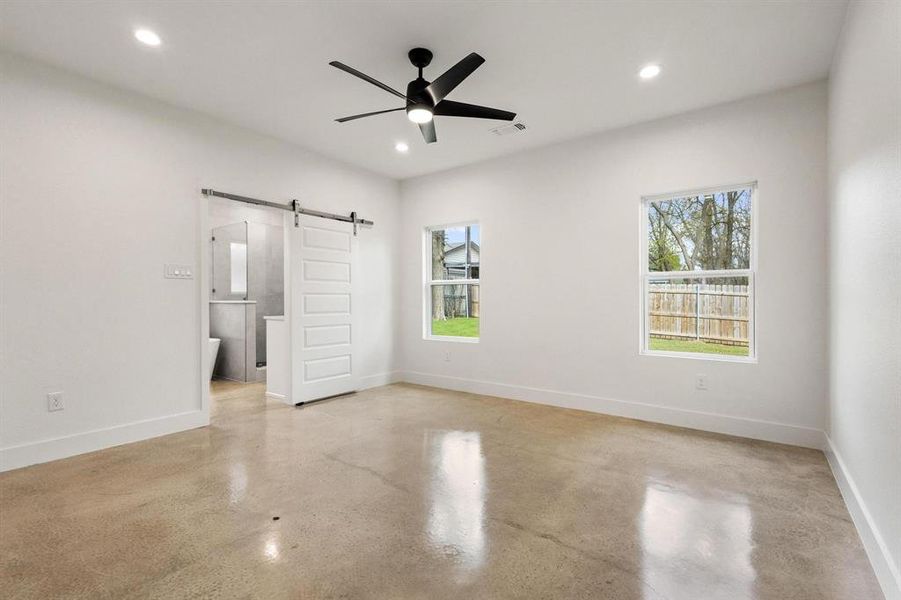 Unfurnished bedroom featuring a barn door, concrete flooring, a ceiling fan, recessed lighting, and connected bathroom