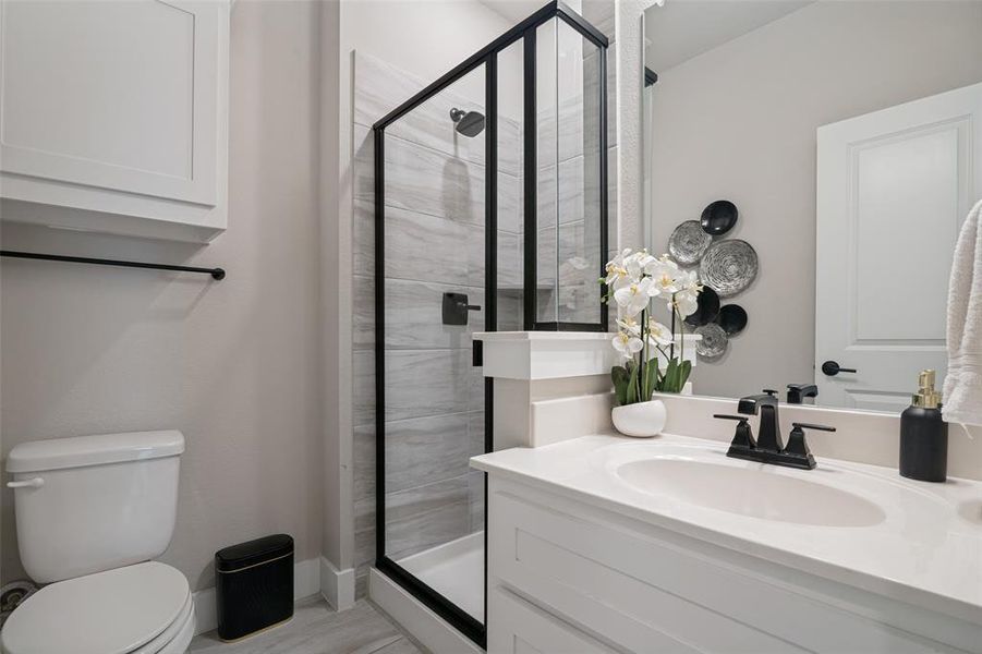 Bathroom featuring a framed glass shower enclosure, a vanity with an integrated sink, a built-in wall cabinet, and a white toilet