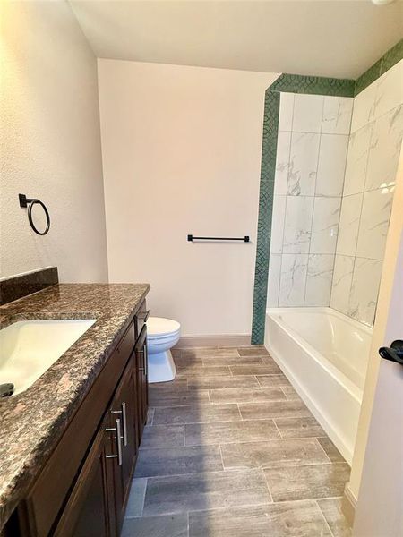 Bathroom featuring wood-finish tile flooring, a dark wood-finish vanity with an undermount sink and stone countertop, and a tiled tub/shower combination with decorative accent tile Bathroom featuring wood-finish tile flooring, a dark wood-finish vanity with an undermount sink and stone countertop, and a tiled tub/shower combination with decorative accent tile