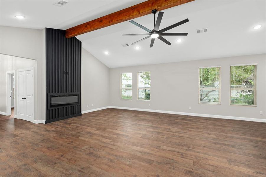 Unfurnished living room with beamed ceiling, a glass covered fireplace, dark wood-style flooring, recessed lighting, and ceiling fan