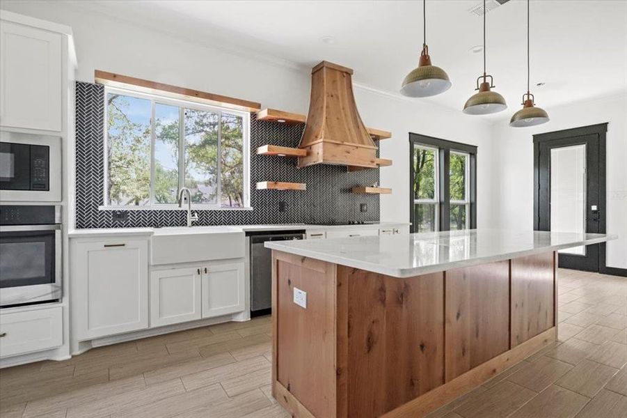 Kitchen featuring tasteful backsplash, white cabinetry, decorative light fixtures, stainless steel appliances, and a kitchen island