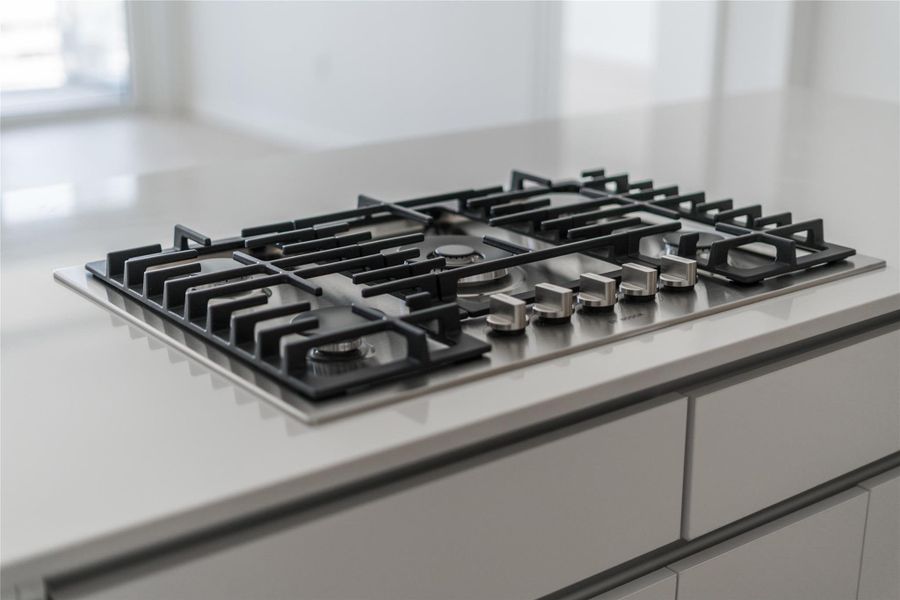 A modern gas cooktop, sleekly integrated into light-toned countertops, awaits culinary endeavors. A modern gas cooktop, sleekly integrated into light-toned countertops, awaits culinary endeavors.