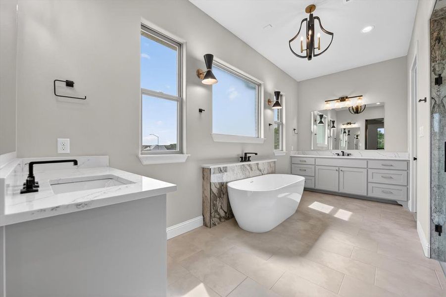 Spacious bathroom featuring a freestanding tub, dual vanity with quartz countertops, custom cabinetry, and large format floor tile
