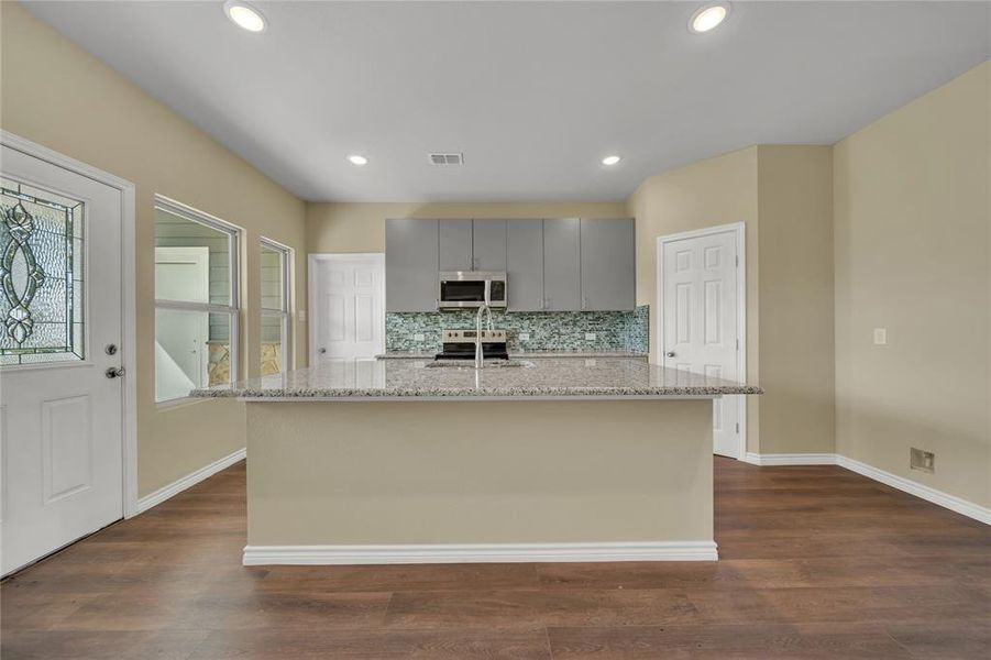 Kitchen featuring dark hardwood / wood-style flooring, appliances with stainless steel finishes, gray cabinets, and backsplash