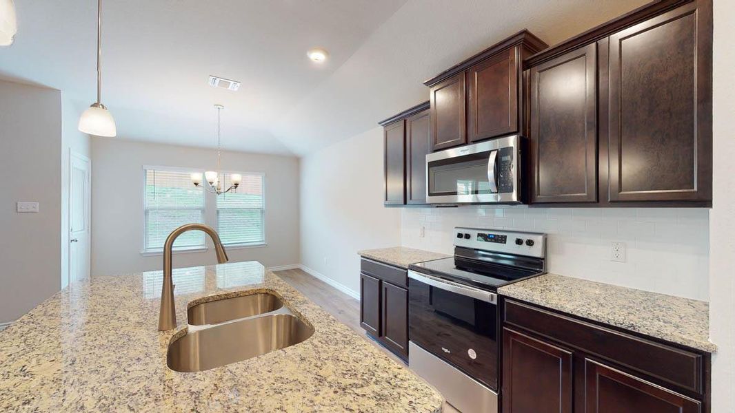 Kitchen featuring stainless steel appliances, dark wood finish cabinetry, light stone countertops, light wood-style flooring, and suspended lighting