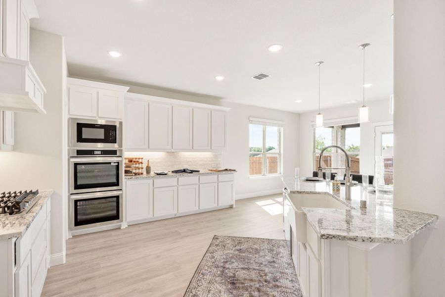 Kitchen with white cabinets, granite island, stainless steel double ovens, and hardwood floors