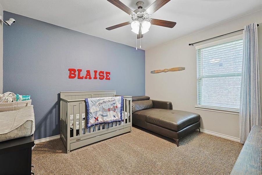 Carpeted bedroom featuring multiple windows, a nursery area, and ceiling fan