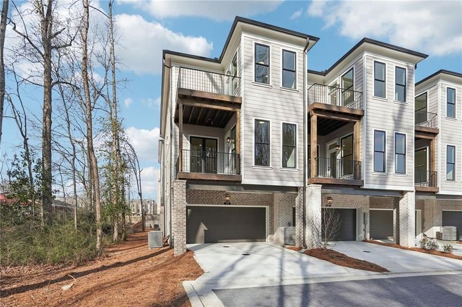 View of back of property with the back decks off the main level and primary bedroom on top level. The views off the back of this building overlook the wooded green space with walking path in the community!