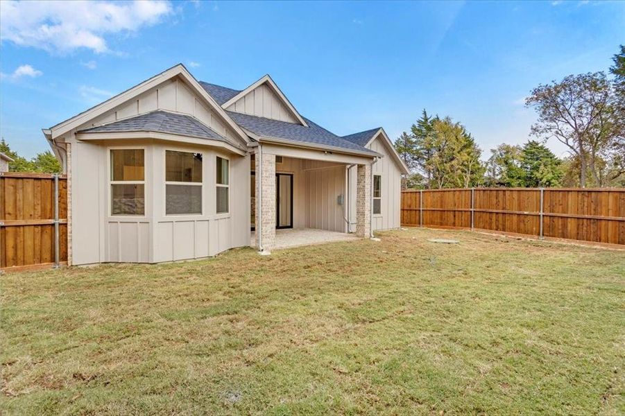 Rear view of house featuring board and batten siding, a patio area, a shingled roof, and a fenced backyard