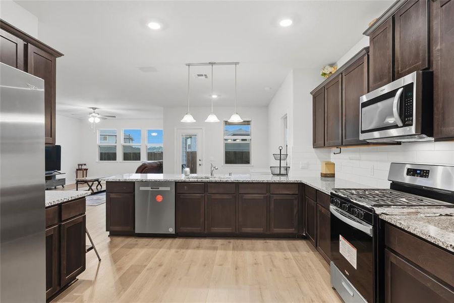 Modern kitchen featuring dark wood-finish cabinetry, light wood-finish flooring, and a white subway tile backsplash