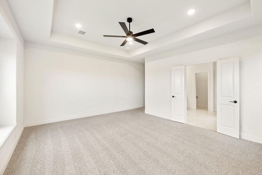 Empty bedroom with tray ceiling, ceiling fan, carpet flooring, and two white doors Empty bedroom with tray ceiling, ceiling fan, carpet flooring, and two white doors