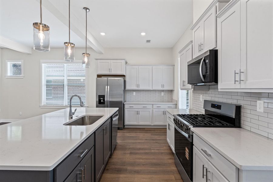 Two tone kitchen with stainless steel appliances, a kitchen island with sink, two tone cabinets, decorative light fixtures, and dark wood finished floors Two tone kitchen with stainless steel appliances, a kitchen island with sink, two tone cabinets, decorative light fixtures, and dark wood finished floors