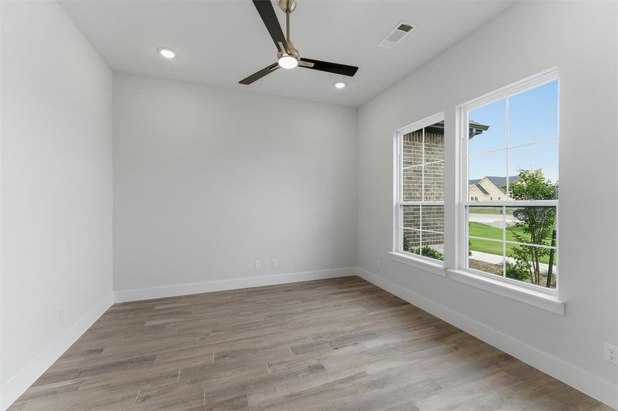 Bright room featuring two windows, wood-finish flooring, a ceiling fan with integrated lighting, and recessed ceiling lights