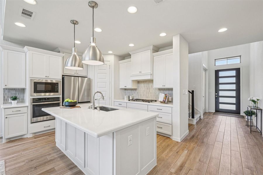 The kitchen features white cabinetry, stainless steel appliances, a white island with an integrated sink, and recessed lighting