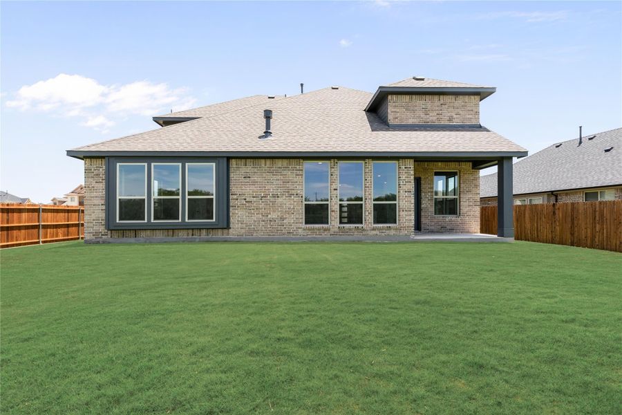 Rear view of brick home with large windows, covered patio, and fenced backyard with green lawn Rear view of brick home with large windows, covered patio, and fenced backyard with green lawn