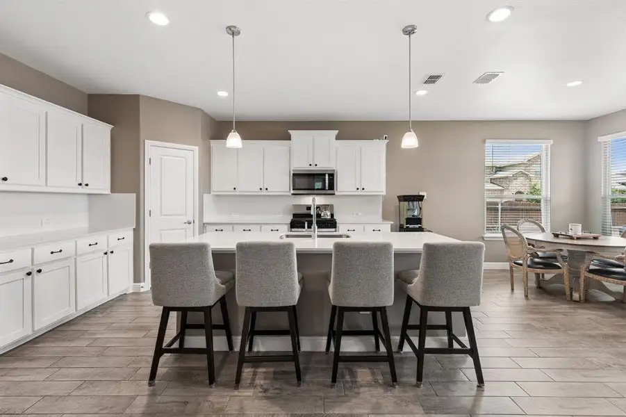 Expansive kitchen featuring a large central island, white cabinetry, integrated stainless steel microwave, recessed lighting, and wood-finish flooring