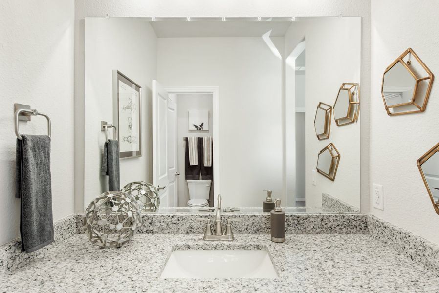 Bathroom vanity with granite countertop, undermount sink, large mirror, and gold geometric wall shelves