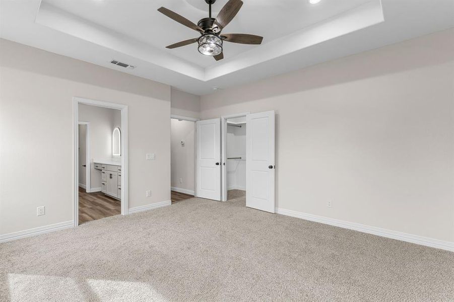 Unfurnished bedroom featuring a raised ceiling, dark colored carpet, a spacious closet, and ensuite bath Unfurnished bedroom featuring a raised ceiling, dark colored carpet, a spacious closet, and ensuite bath