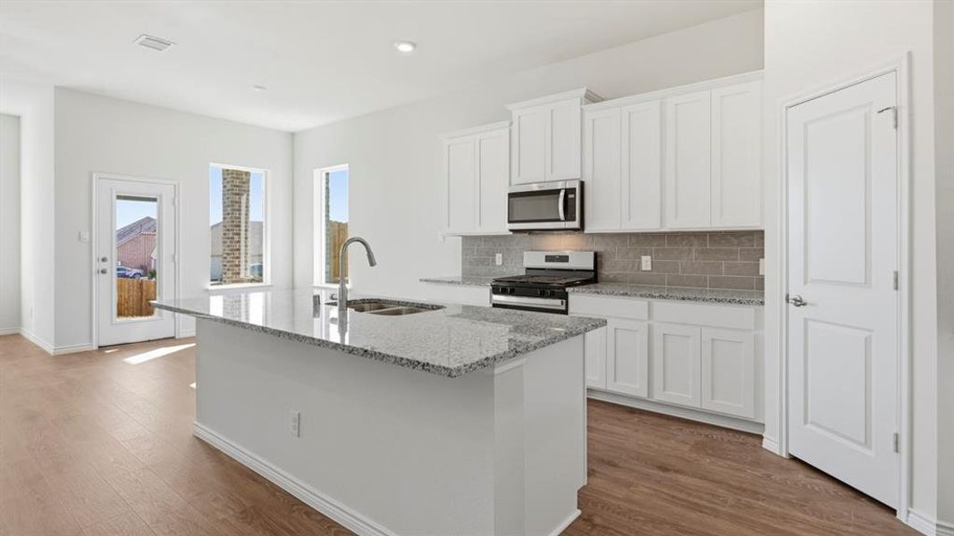 Kitchen with light stone counters, white cabinets, backsplash, range with gas stovetop, and a center island with sink Kitchen with light stone counters, white cabinets, backsplash, range with gas stovetop, and a center island with sink