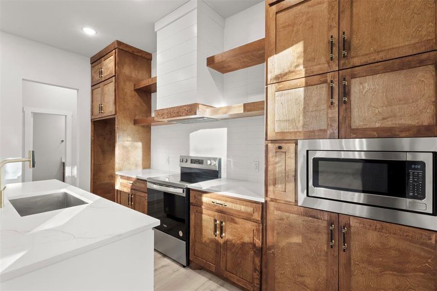 Kitchen featuring sink, light hardwood / wood-style flooring, decorative backsplash, light stone countertops, and appliances with stainless steel finishes