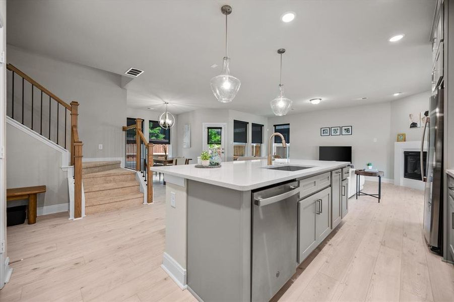 Kitchen with appliances with stainless steel finishes, open floor plan, gray cabinets, light countertops, and a kitchen island with sink Kitchen with appliances with stainless steel finishes, open floor plan, gray cabinets, light countertops, and a kitchen island with sink