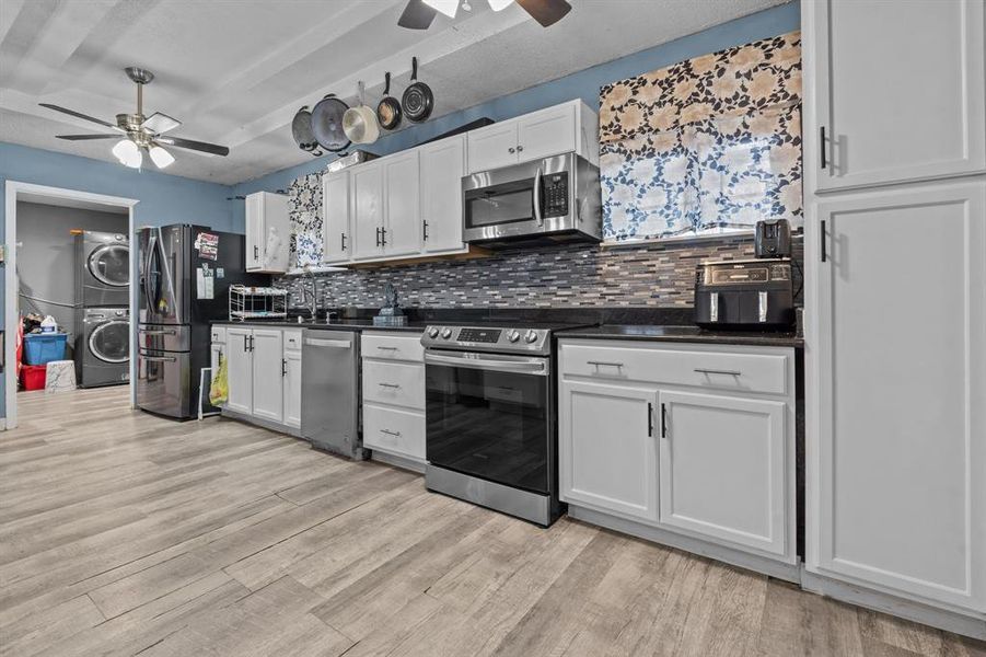 Kitchen with ceiling fan, tasteful backsplash, stacked washing maching and dryer, stainless steel appliances, and white cabinets