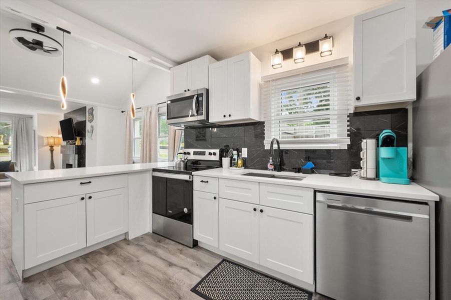 Kitchen featuring appliances with stainless steel finishes, a peninsula, light wood-style flooring, white cabinetry, and decorative backsplash Kitchen featuring appliances with stainless steel finishes, a peninsula, light wood-style flooring, white cabinetry, and decorative backsplash