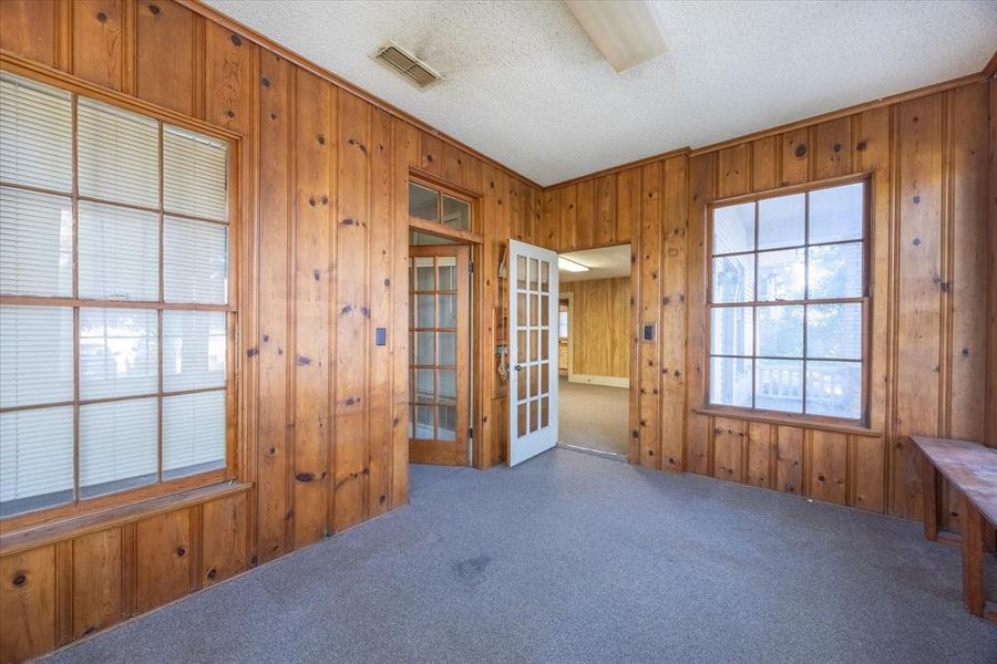 Spare room with french doors, a textured ceiling, carpet floors, ornamental molding, and wood walls