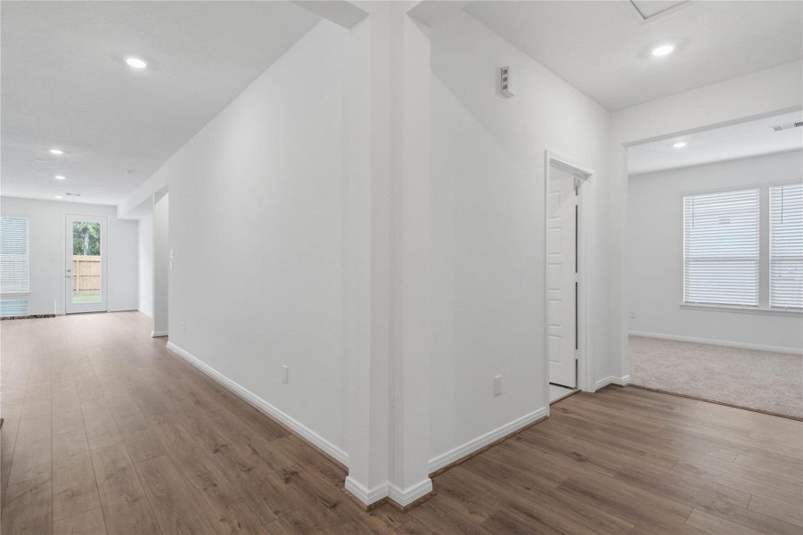 The functional main hallway transitions seamlessly into a private wing, leading back to a secluded den or home office space. This central artery features rich vinyl plank flooring, crisp white trim, and bright recessed lighting that illuminates the path to both the living areas and the Den.