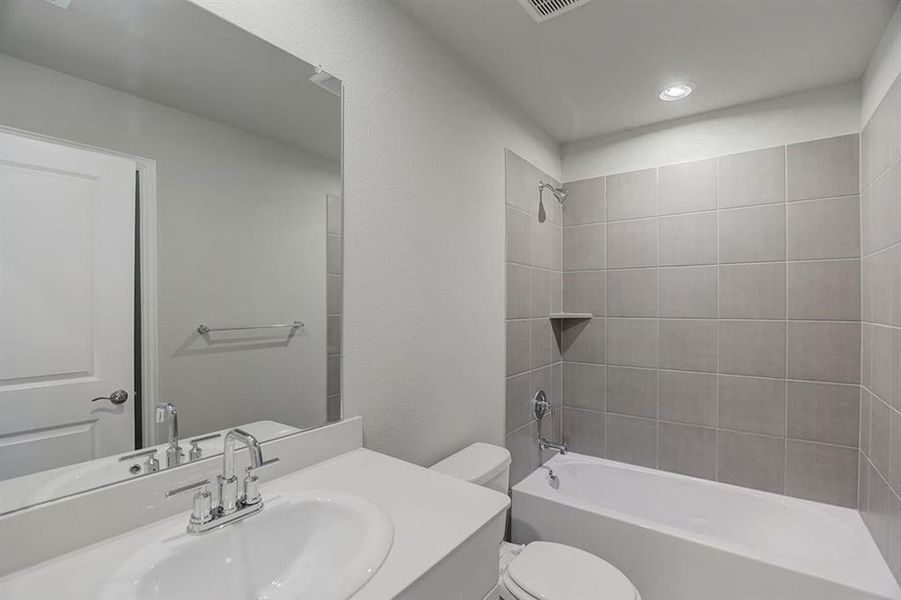 Full bathroom featuring vanity, tiled shower / bath, and toilet