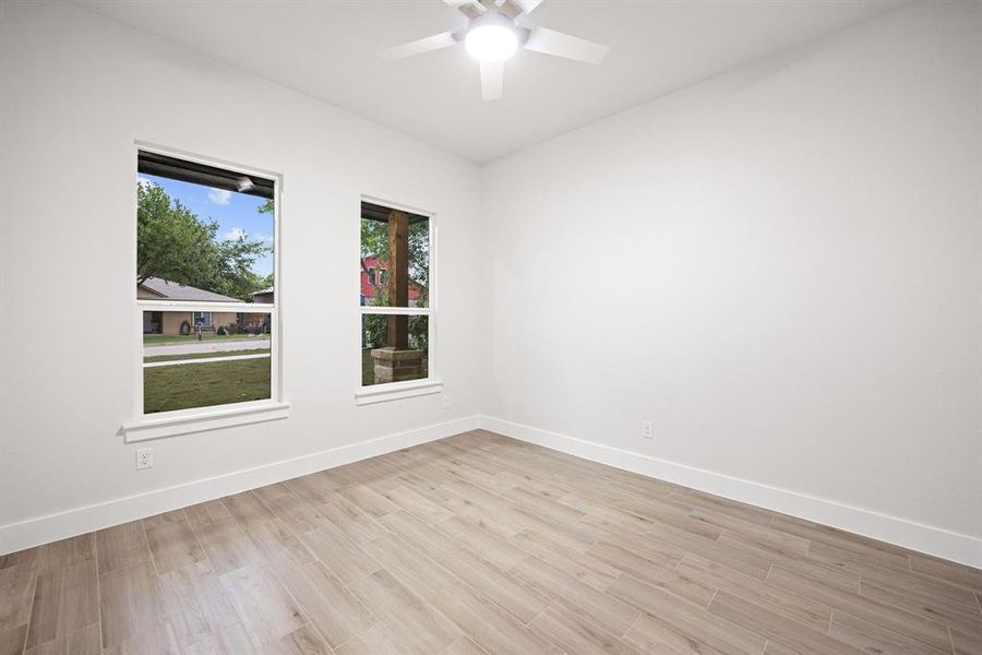Bright room featuring two windows, wood-finish flooring, a ceiling fan with integrated lighting, and white baseboards Bright room featuring two windows, wood-finish flooring, a ceiling fan with integrated lighting, and white baseboards