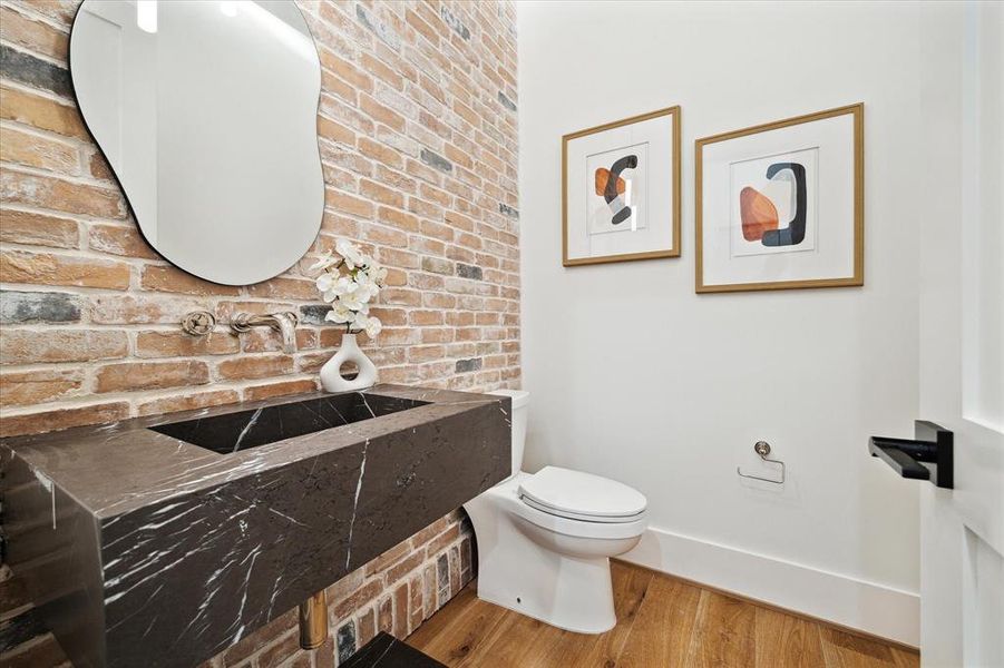 Featuring marble countertops with an integrated sink and complemented by a wall mounted polished nickel faucet, the bathroom boasts an elegant touch. a brick accent wall adds character, while a signature hardware commode provides functionality. The space is finished with 7" European engineered white oak flooring and illuminated by a visual comfort lighting pendant, creating a sophisticated atmosphere.