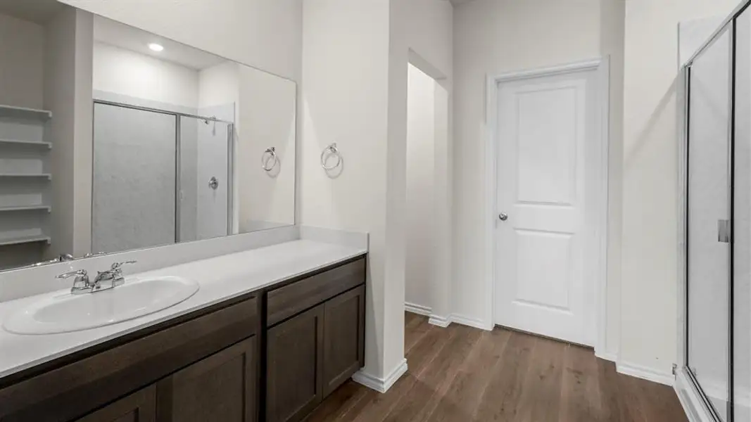 Bathroom featuring a spacious vanity with an integrated sink and ample storage, a large mirror, and a shower with a sliding glass door
