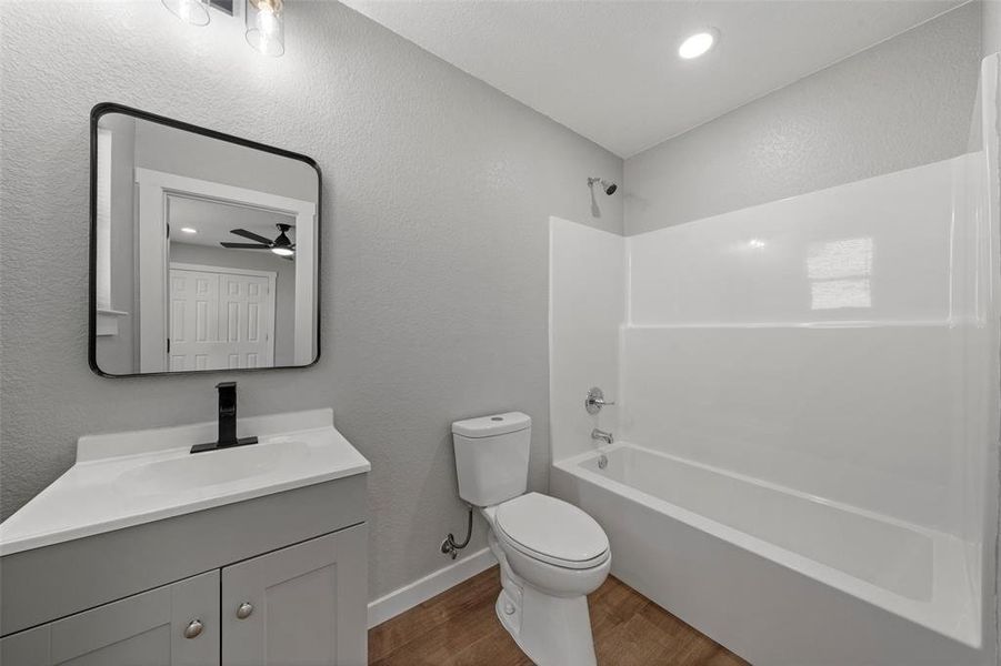 Full bath featuring wood finished floors, vanity, shower / tub combination, ceiling fan, and a textured wall Full bath featuring wood finished floors, vanity, shower / tub combination, ceiling fan, and a textured wall