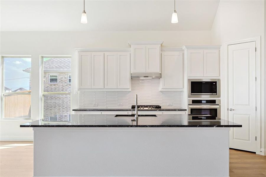 Kitchen featuring a center island with sink, stainless steel appliances, light hardwood / wood-style floors, and decorative light fixtures