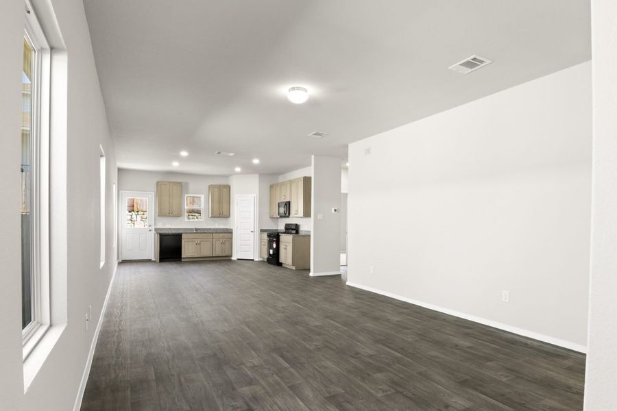 Image of a one story house living room with dark wood-like flooring and light grey painted walls with a kitchen in the distance Image of a one story house living room with dark wood-like flooring and light grey painted walls with a kitchen in the distance