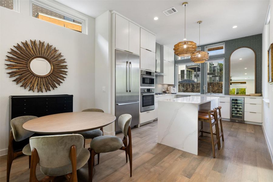 Kitchen featuring white cabinetry, modern cabinets, light stone counters, beverage cooler, and a kitchen bar