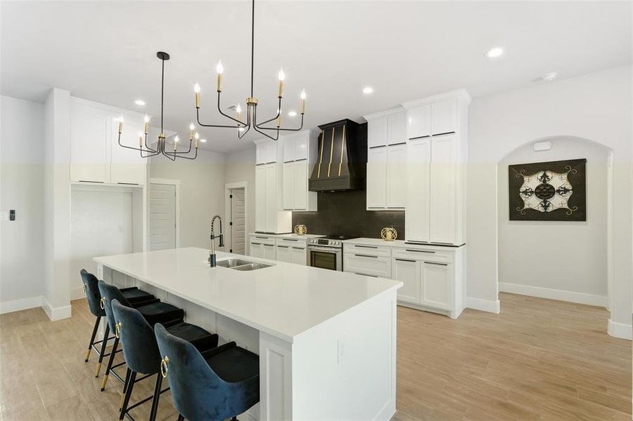 Kitchen featuring a breakfast bar area, custom range hood, white cabinetry, an island with sink, and tasteful backsplash