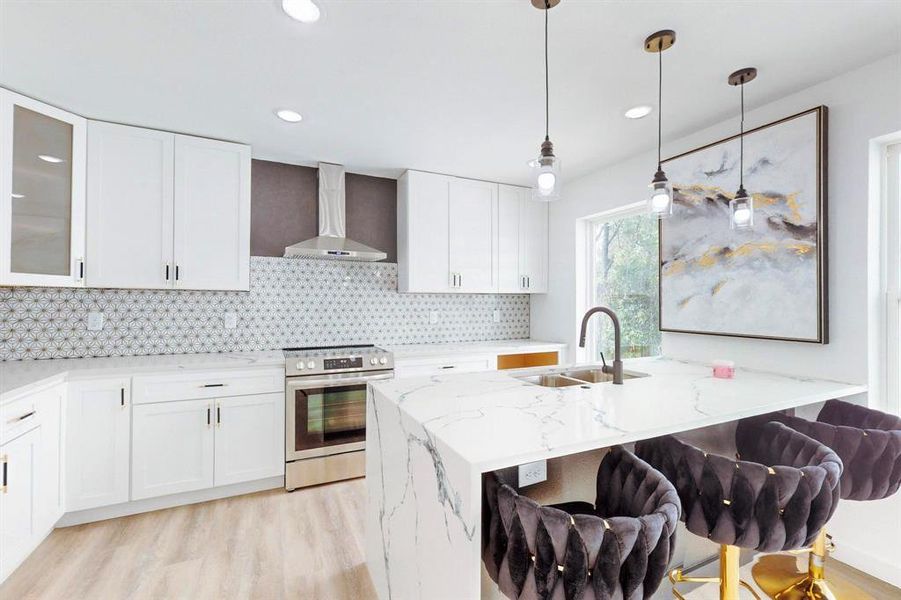 Kitchen featuring wall chimney exhaust hood, stainless steel stove, light stone counters, and a breakfast bar