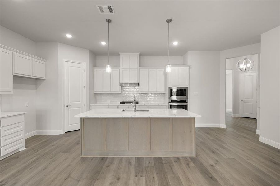 Kitchen featuring stainless steel appliances, decorative backsplash, light wood-style flooring, a center island with sink, and white cabinets Kitchen featuring stainless steel appliances, decorative backsplash, light wood-style flooring, a center island with sink, and white cabinets