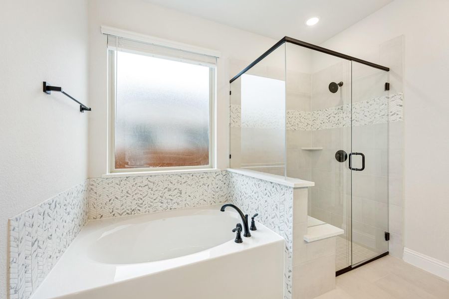 White bathroom with soaking tub, mosaic tile surround, and glass-enclosed walk-in shower with black hardware