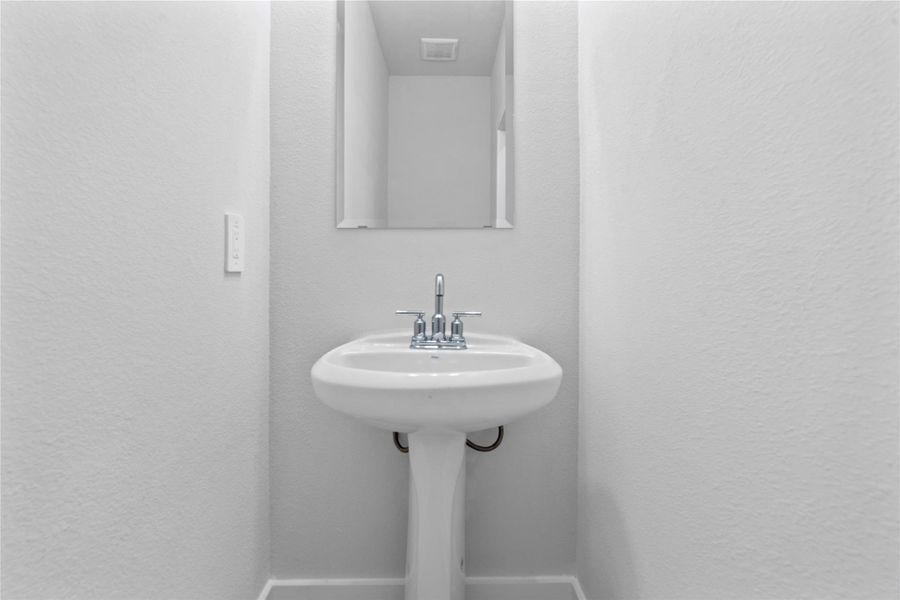 Bright and pristine main-level powder room boasts a crisp color palette, a sleek vanity, and updated fixtures. Perfectly positioned for guest access while maintaining privacy from the main living areas.