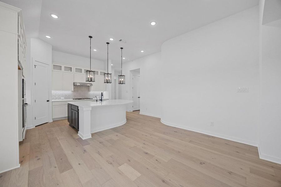 Kitchen with recessed lighting, light countertops, white cabinets, a center island with sink, and light wood-style flooring