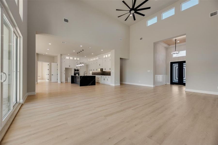 Unfurnished living room with light wood-style flooring, a high ceiling, ceiling fan, and suspended lighting